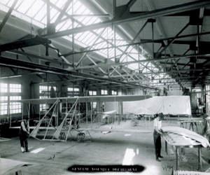 Historic photo showing two men working on an airplane in the interior of the Wright Factory site