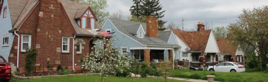 Row of houses with greenery in yards below a cloudy sky in North Central Dayton.