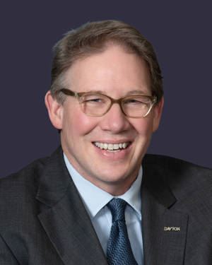 Commissioner Darryl Fairchild smiling in a dark grey suit with a gold pin spelling out Dayton on it.