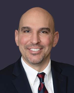 Commissioner Matt Joseph smiling in a dark navy blue suit.