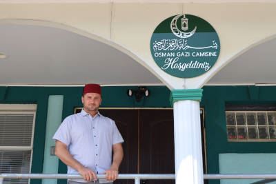 Bayram Gulaliev standing in front of the entrance to a mosque with a green sign above.