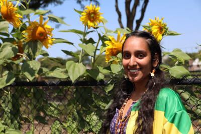 Darsheel Kaur posing for photo in front of chain link fence with tall sunflowers peeking over.