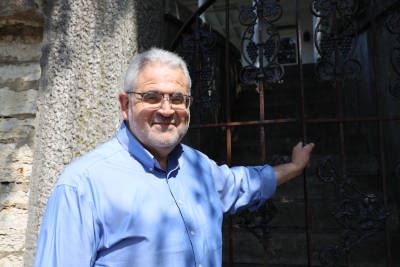 Youssef A. Elzein posing for photo in front of stone wall and wrought iron gate he is holding onto.