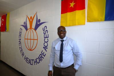 Jean de Dieu Mukunzi posing for photo in front of wall with Ebenezer Healthcare Access logo on it.