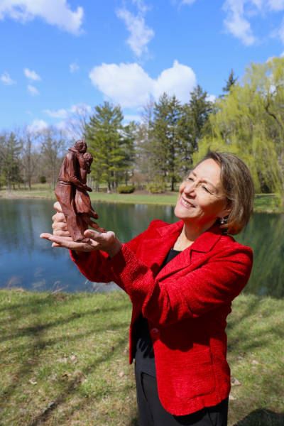 Martha Rodriguez in front of a lake holding a clay statue depicting a woman hugging a man.